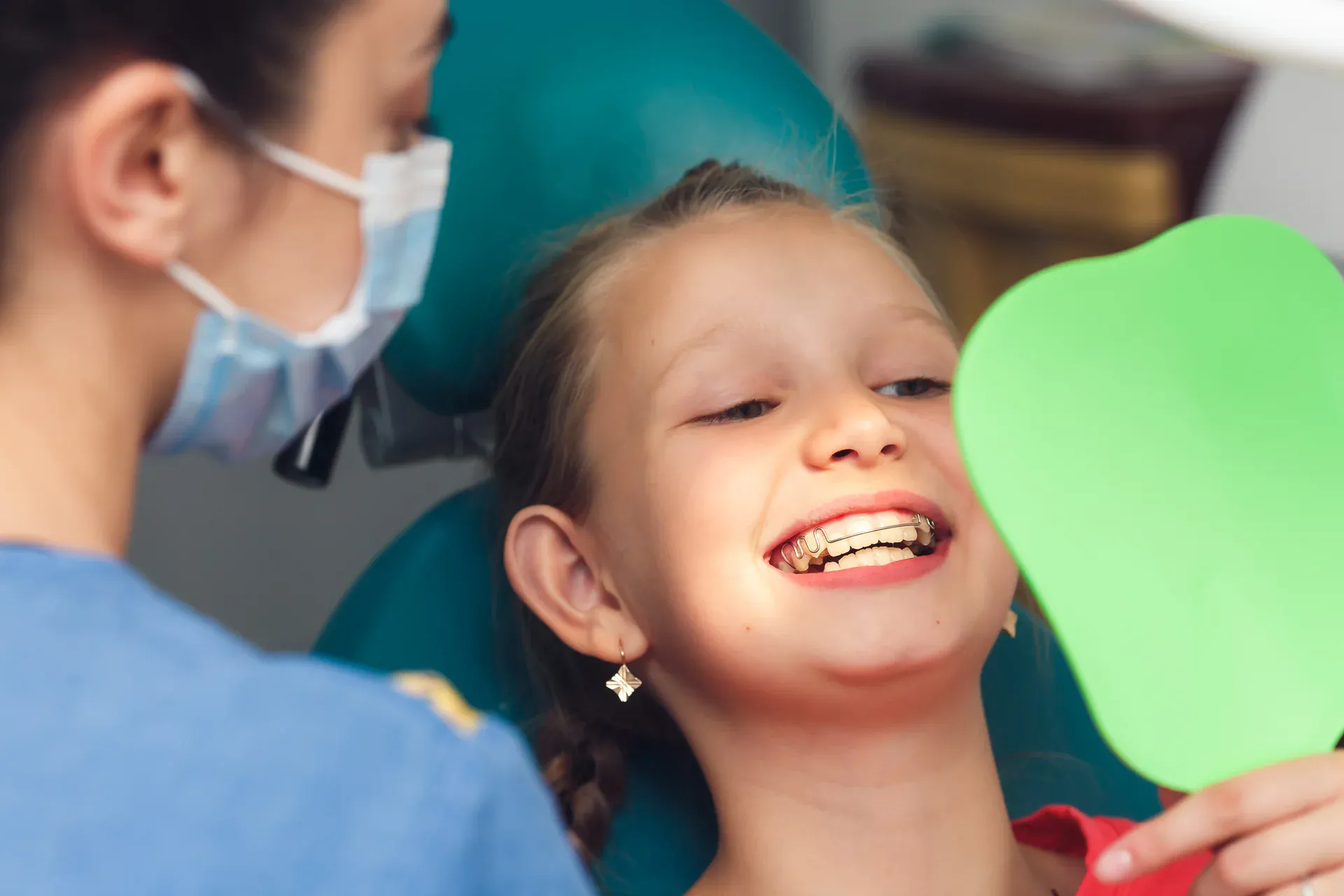 Young girl with orthodontic retainer smiling with dental mirror