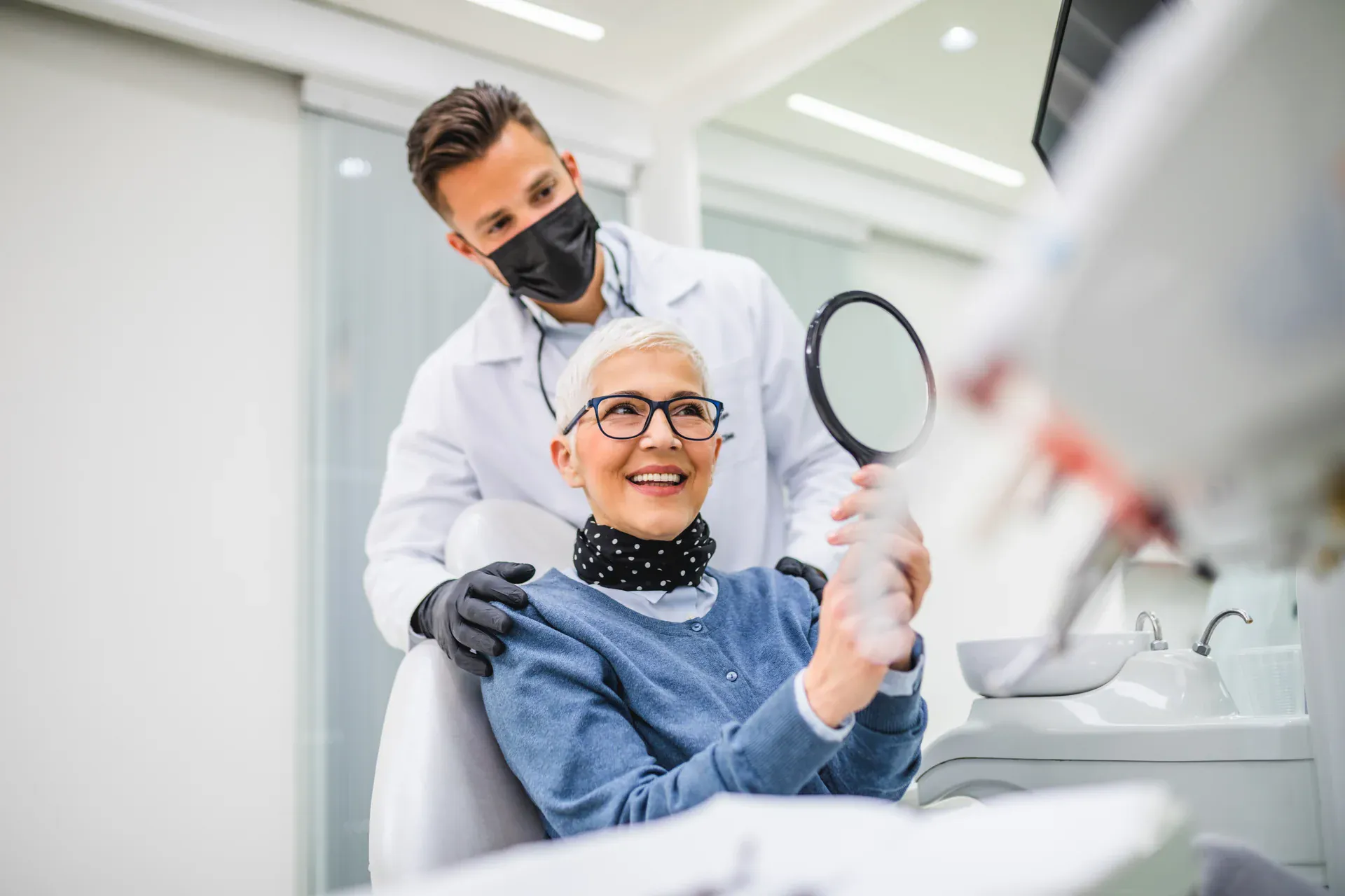 Happy senior patient holding a hand mirror after a dental checkup