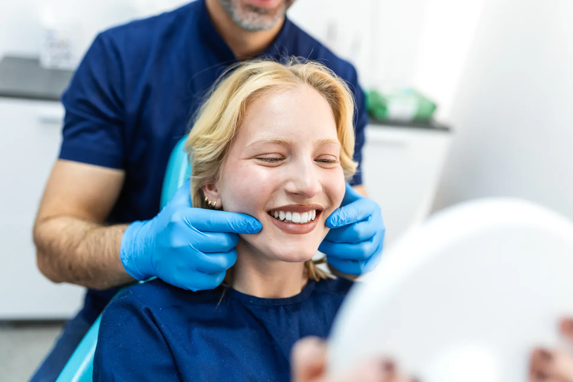 Smiling patient reviewing her smile in a mirror with her dentist