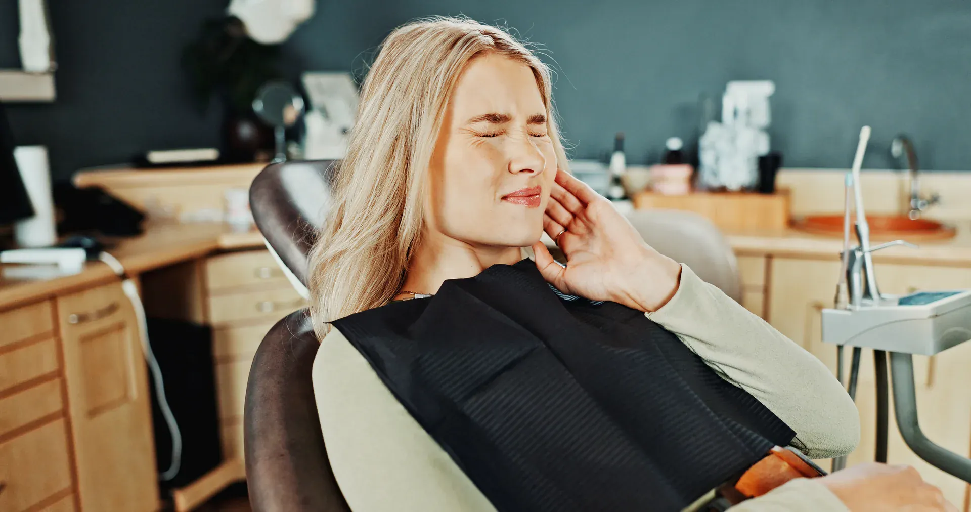 Woman in dental chair holding her jaw with tooth pain