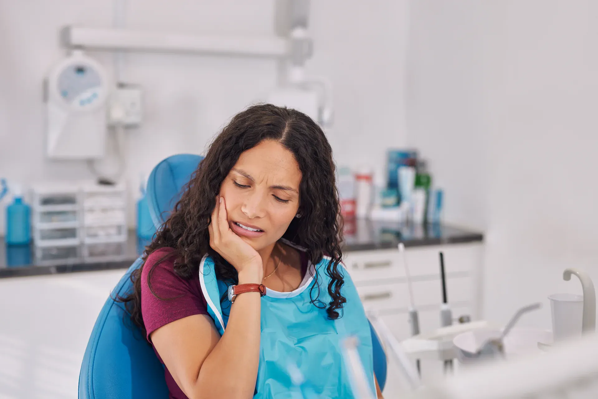 Woman in dental operatory holding her jaw with tooth pain