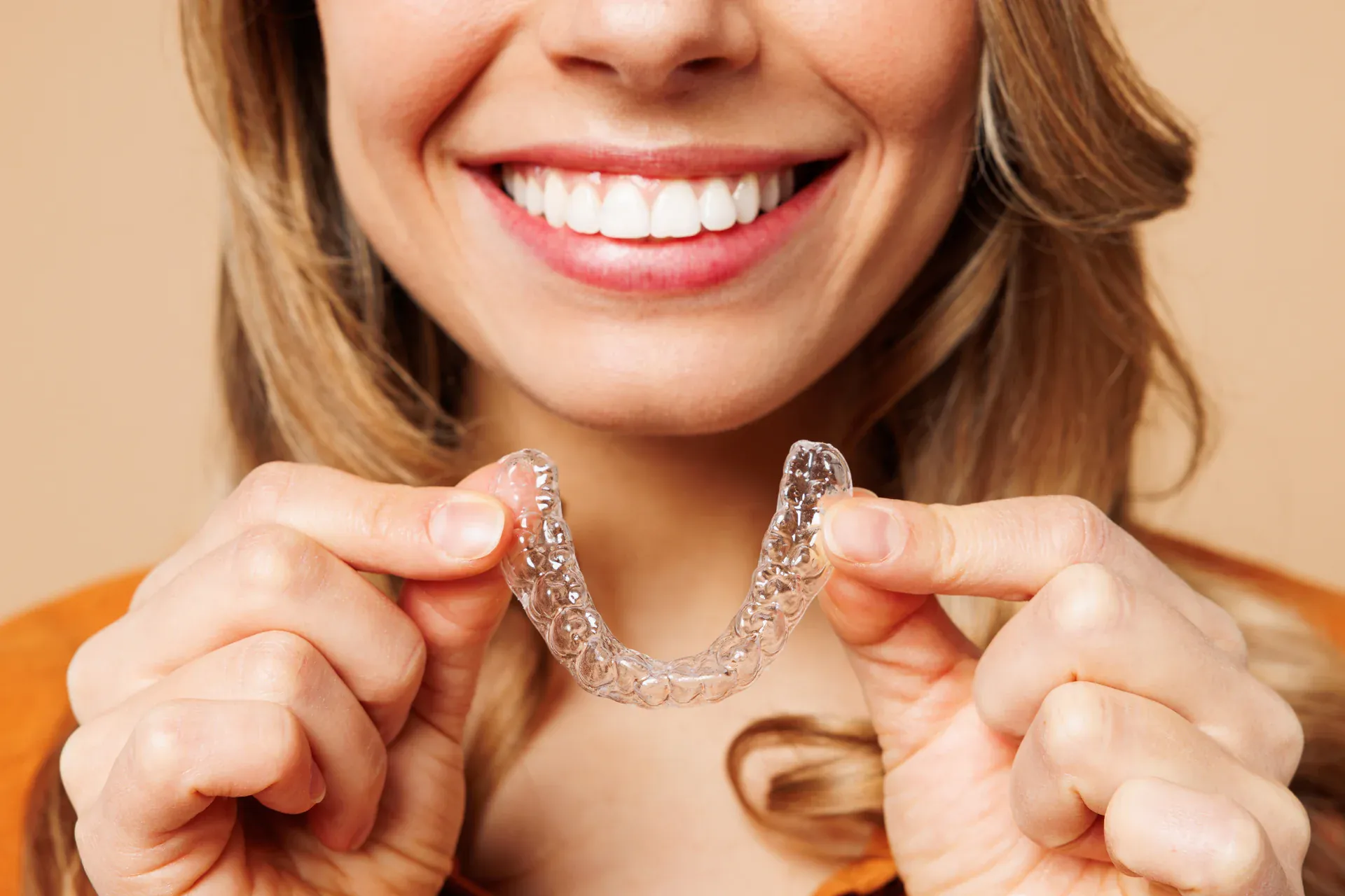 Smiling woman holding a clear Invisalign aligner