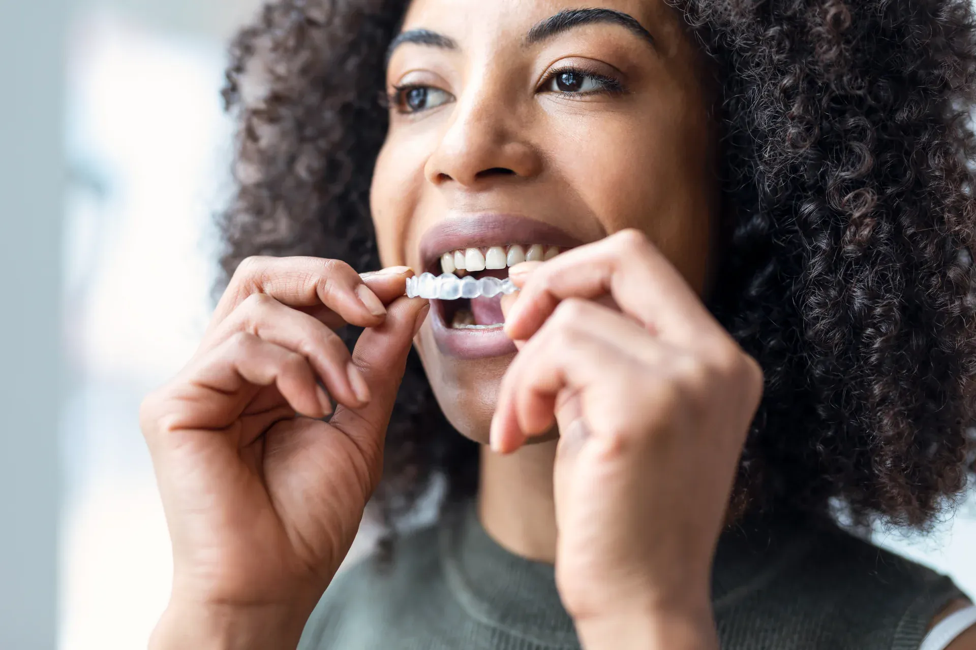 Woman placing a clear Invisalign aligner on her teeth